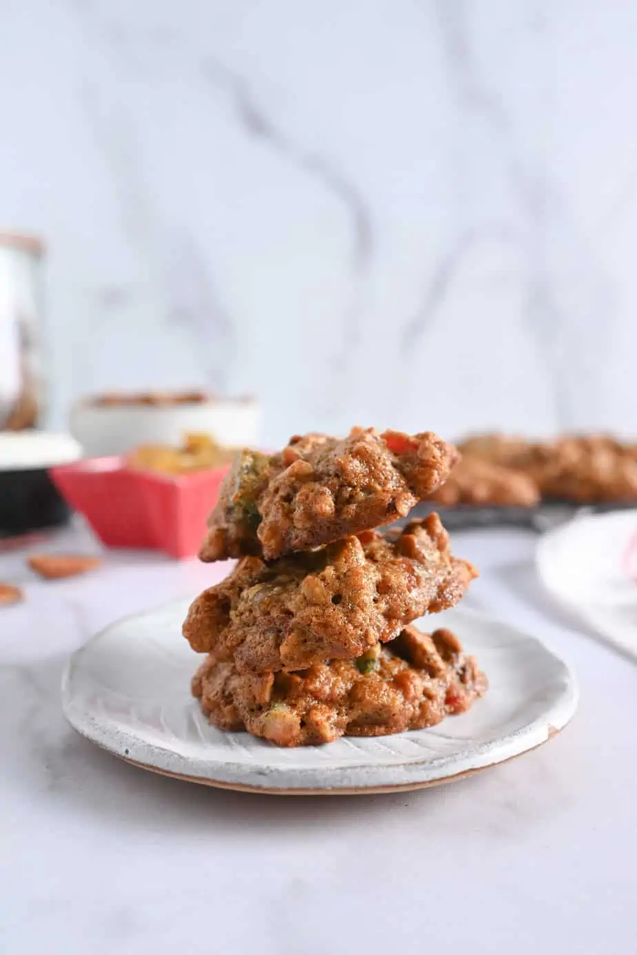 Three fruitcake cookies stacked on a white ceramic plate.