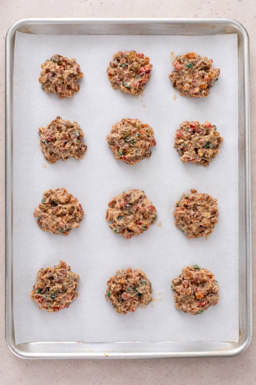 Unbaked fruitcake cookies on a baking sheet, ready to go in the oven.