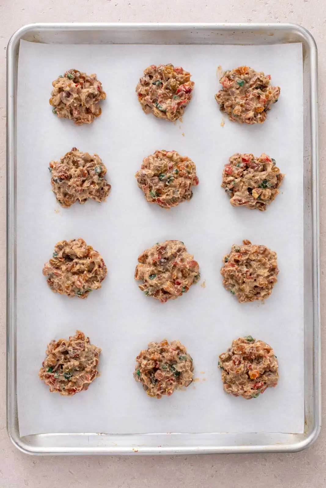 Unbaked fruitcake cookies on a baking sheet, ready to go in the oven.