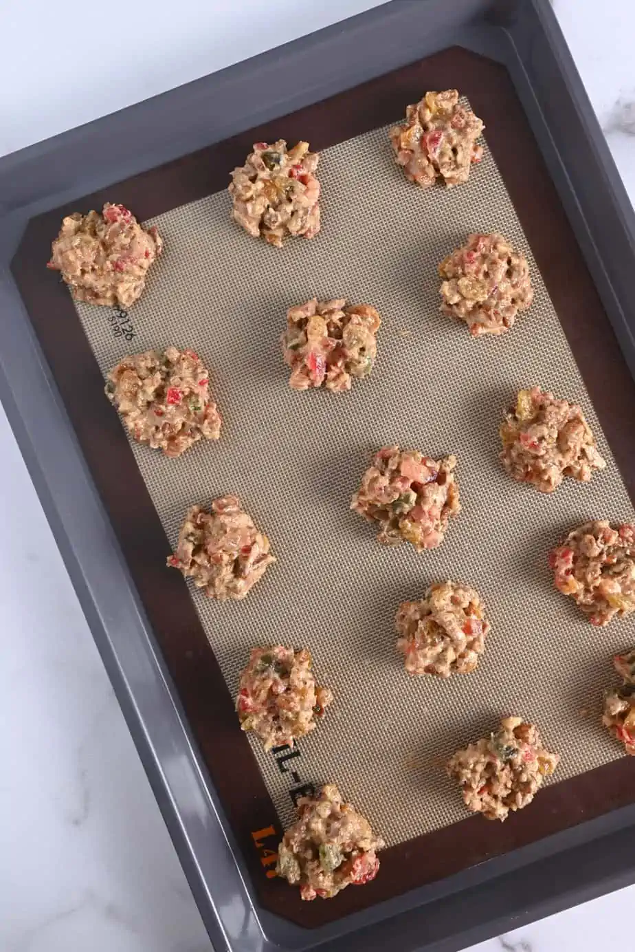 Fruitcake cookie dough portioned onto a lined baking sheet, ready to go in the oven.