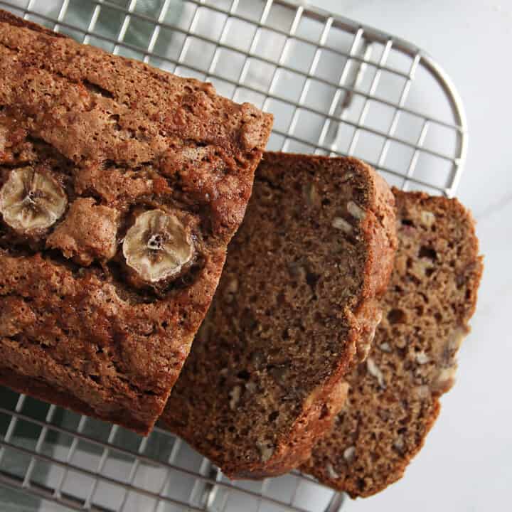Overhead view of sliced loaf of vegan sourdough banana bread on a cooling rack, set on a marble countertop