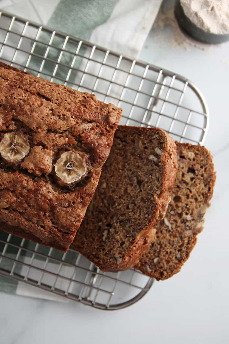 Overhead view of sliced loaf of vegan sourdough banana bread on a cooling rack, set on a marble countertop