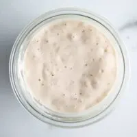 Overhead view of bubbly sourdough starter in a glass jar on a marble counter