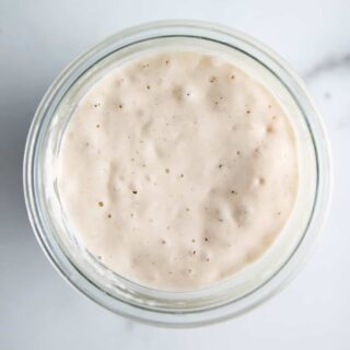 Overhead view of bubbly sourdough starter in a glass jar on a marble counter
