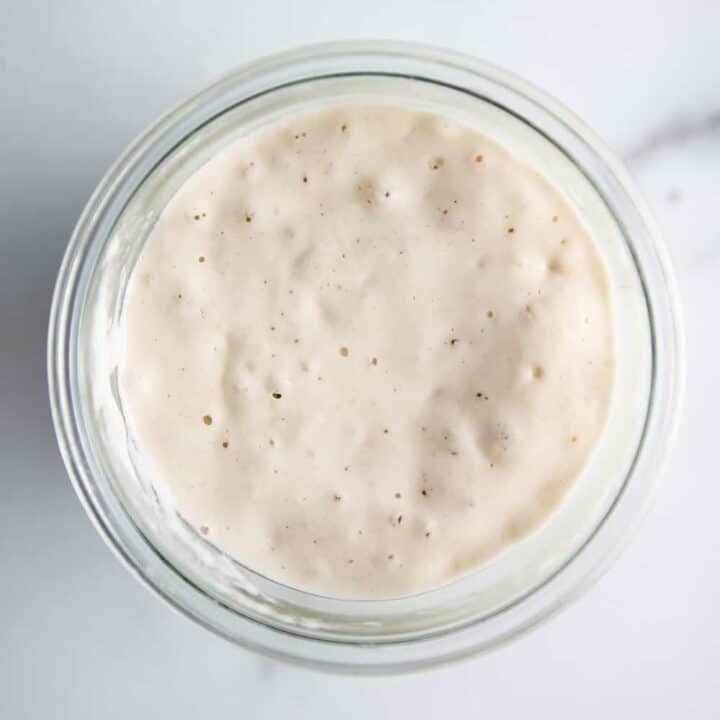 Overhead view of bubbly sourdough starter in a glass jar on a marble counter