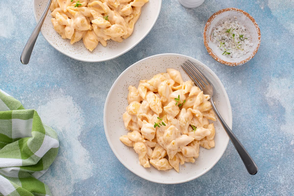 Overhead view of two bowls filled with homemade shells and cheese on a blue countertop.