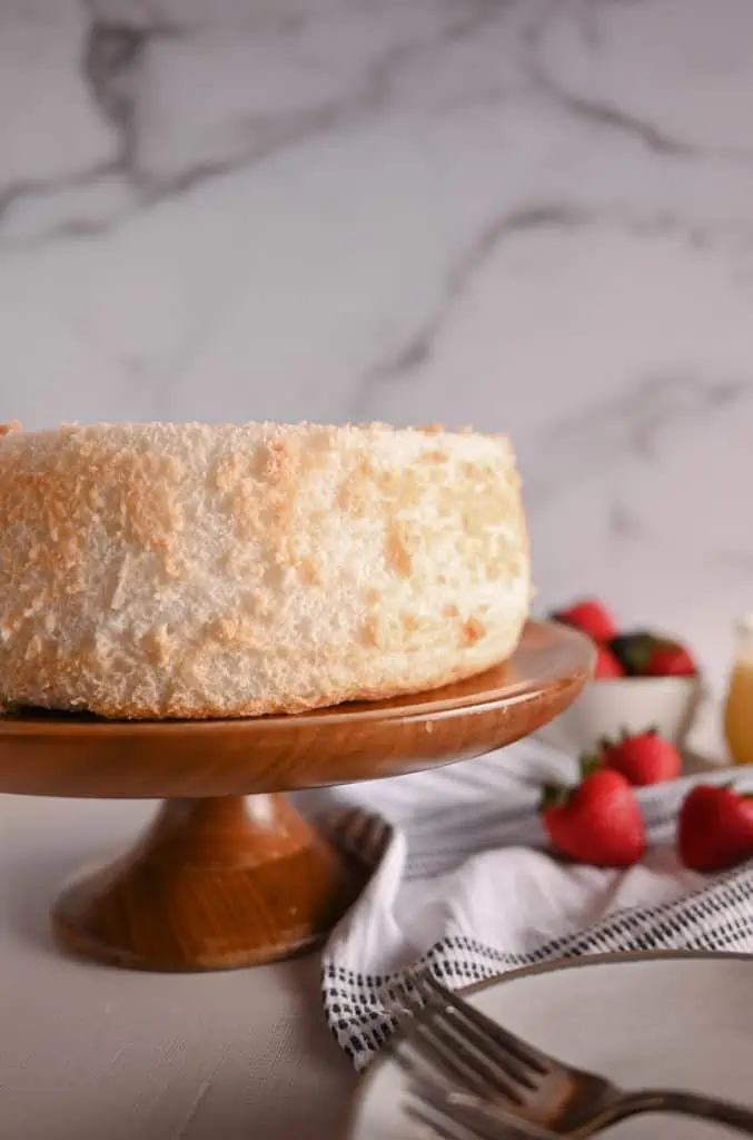 Angel food cake on a wooden cake stand with fresh berries in the background