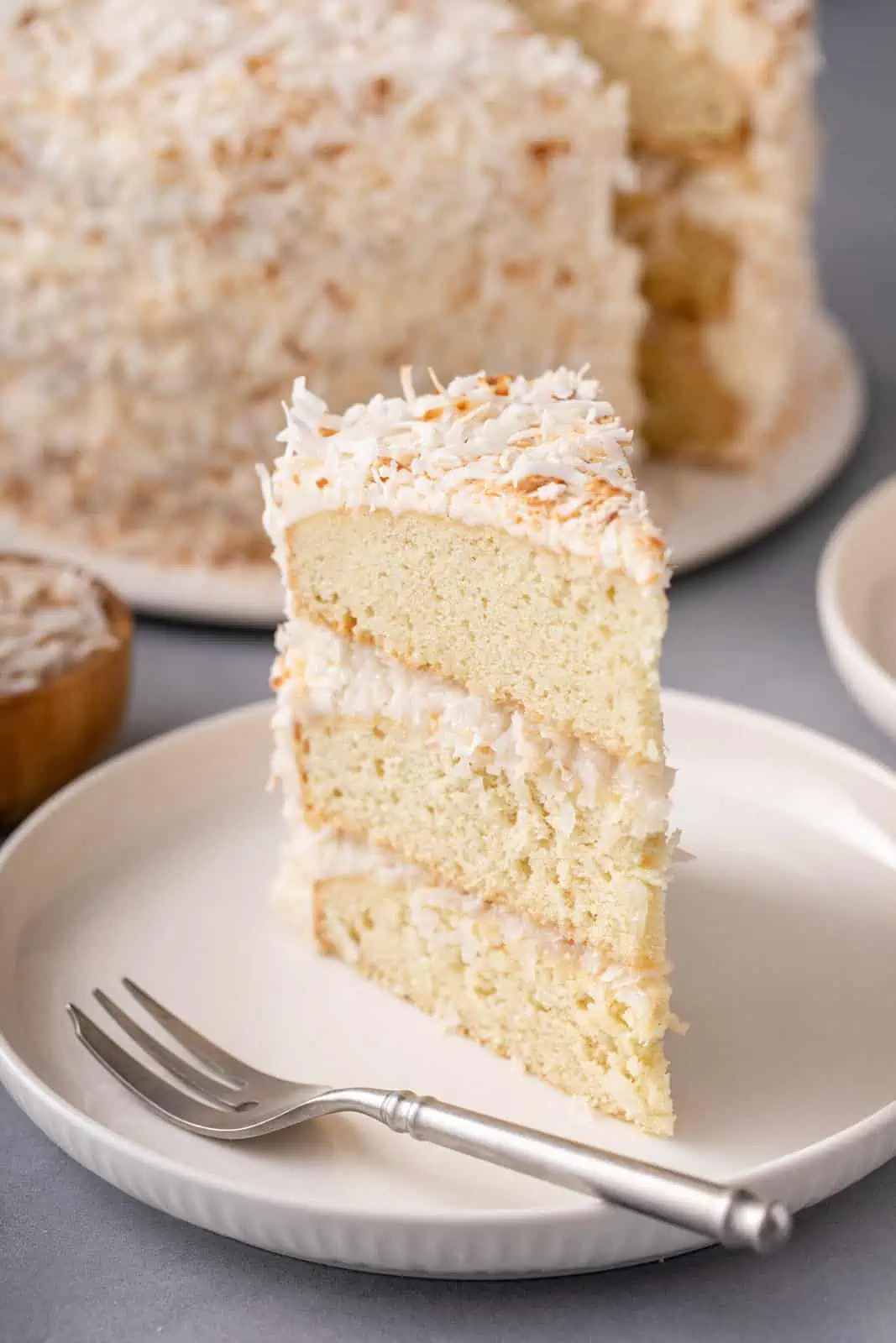 Close up image of a slice of coconut cake on a white plate.