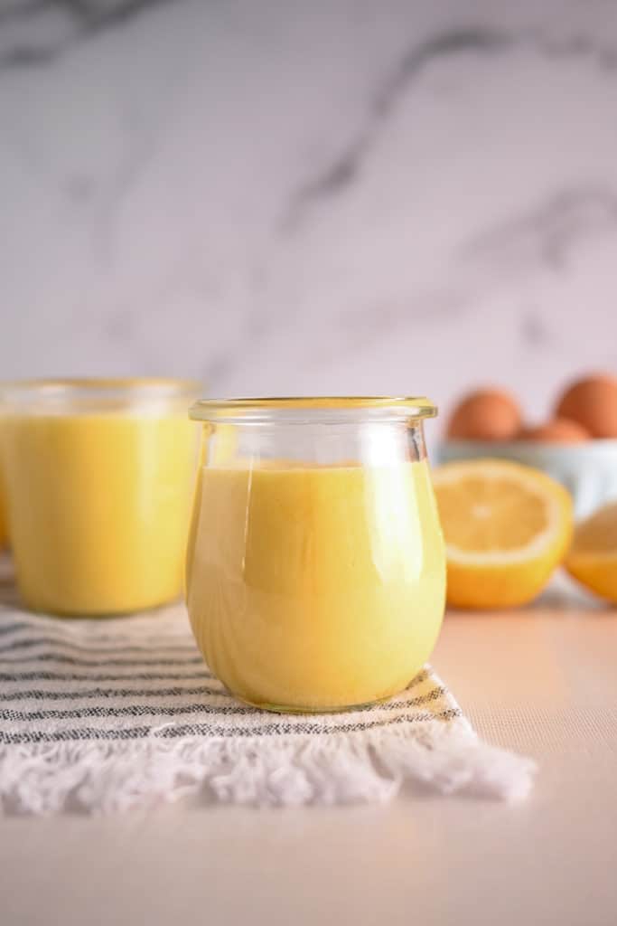 Jar of lemon curd with another jar and cut lemons in the background