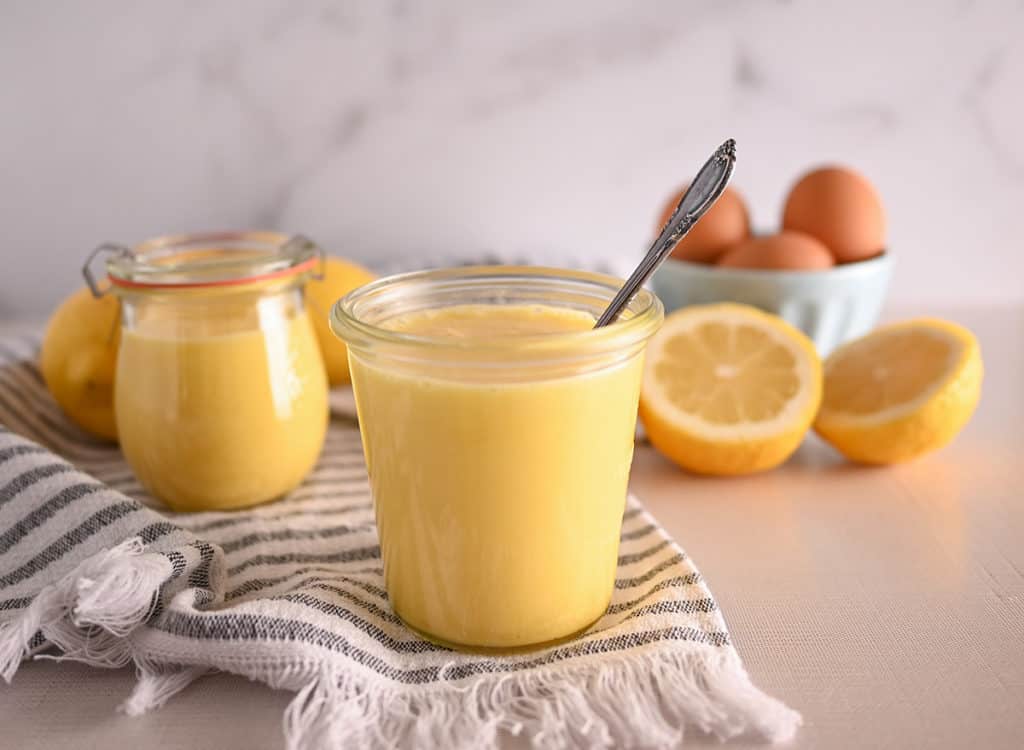 Jars of lemon curd with lemons and eggs in the background
