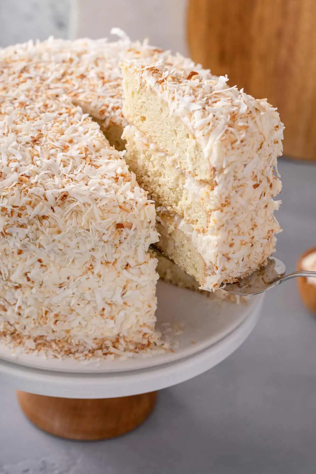 Cake server lifting a slice of coconut cake from the cake stand with the rest of the cake.