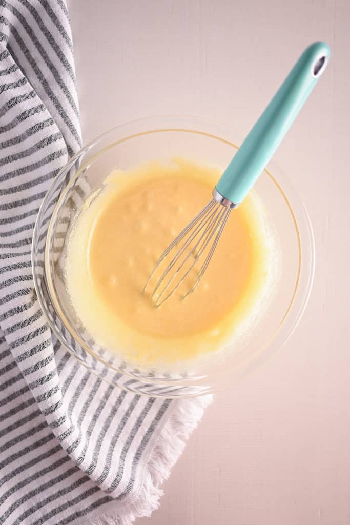 Eggs and sugar being whisked together in a glass bowl