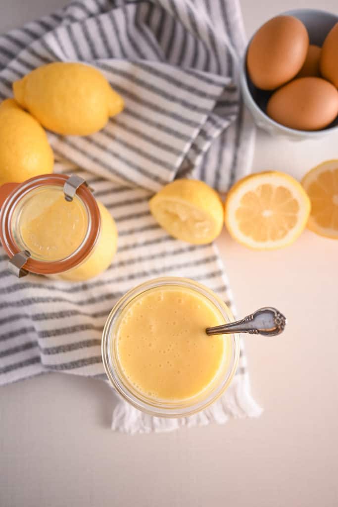 Overhead view of two jars of lemon curd surrounded by cut lemons and eggs