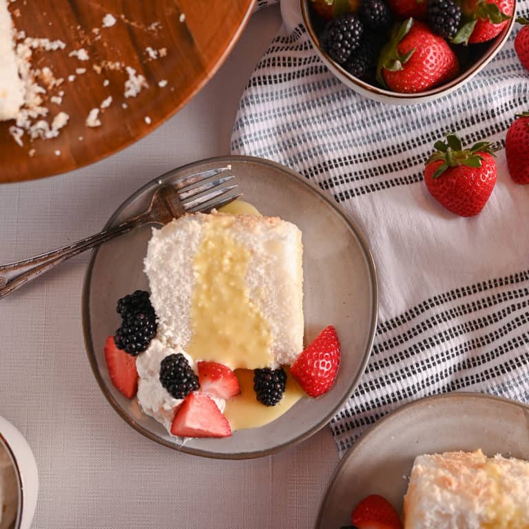 Overhead view of a plated slice of angel food cake, topped with lemon curd and fresh berries