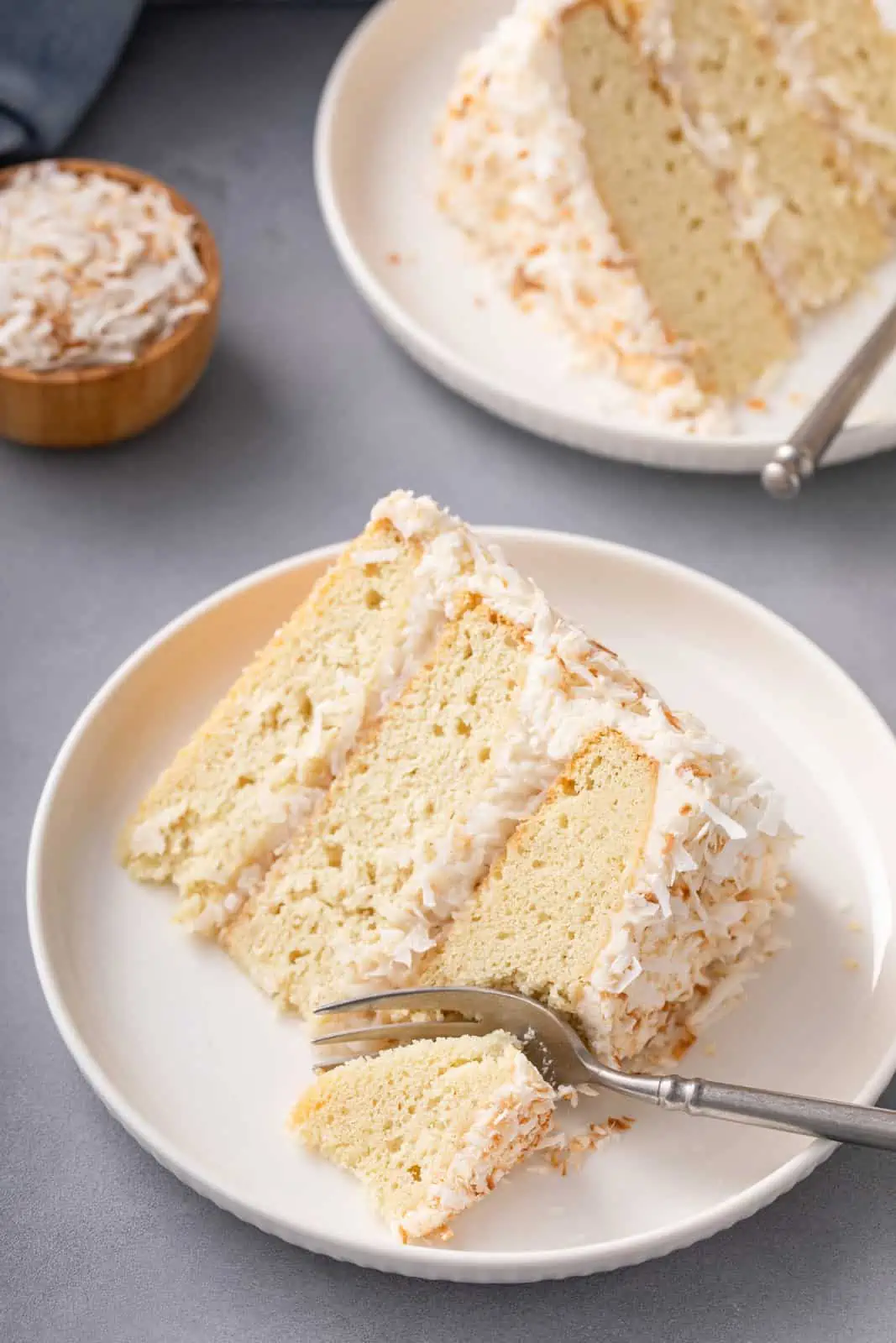 Fork cutting a bite from a slice of coconut cake on a white plate.