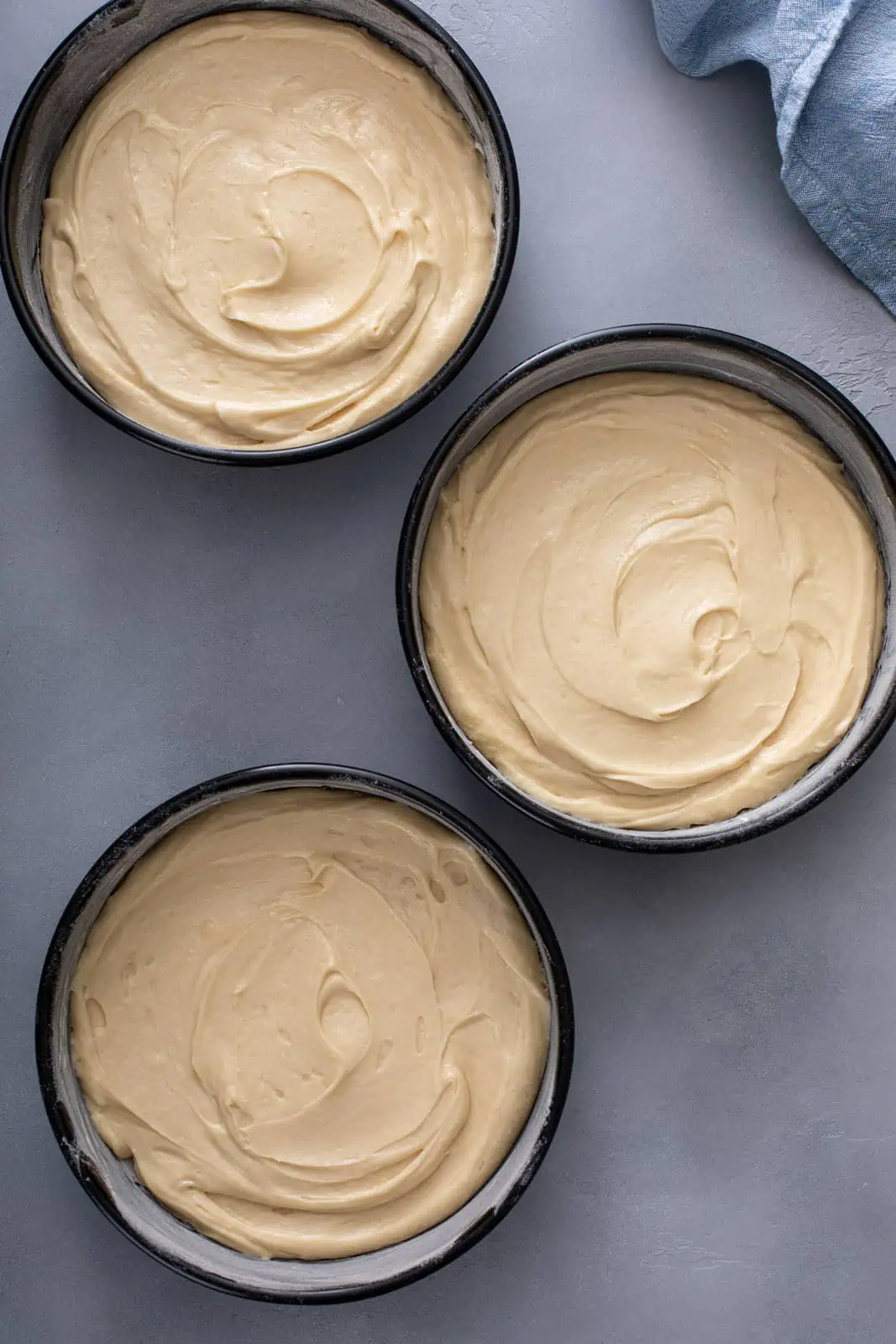 Unbaked coconut cake layers in three cake pans, ready to go in the oven.