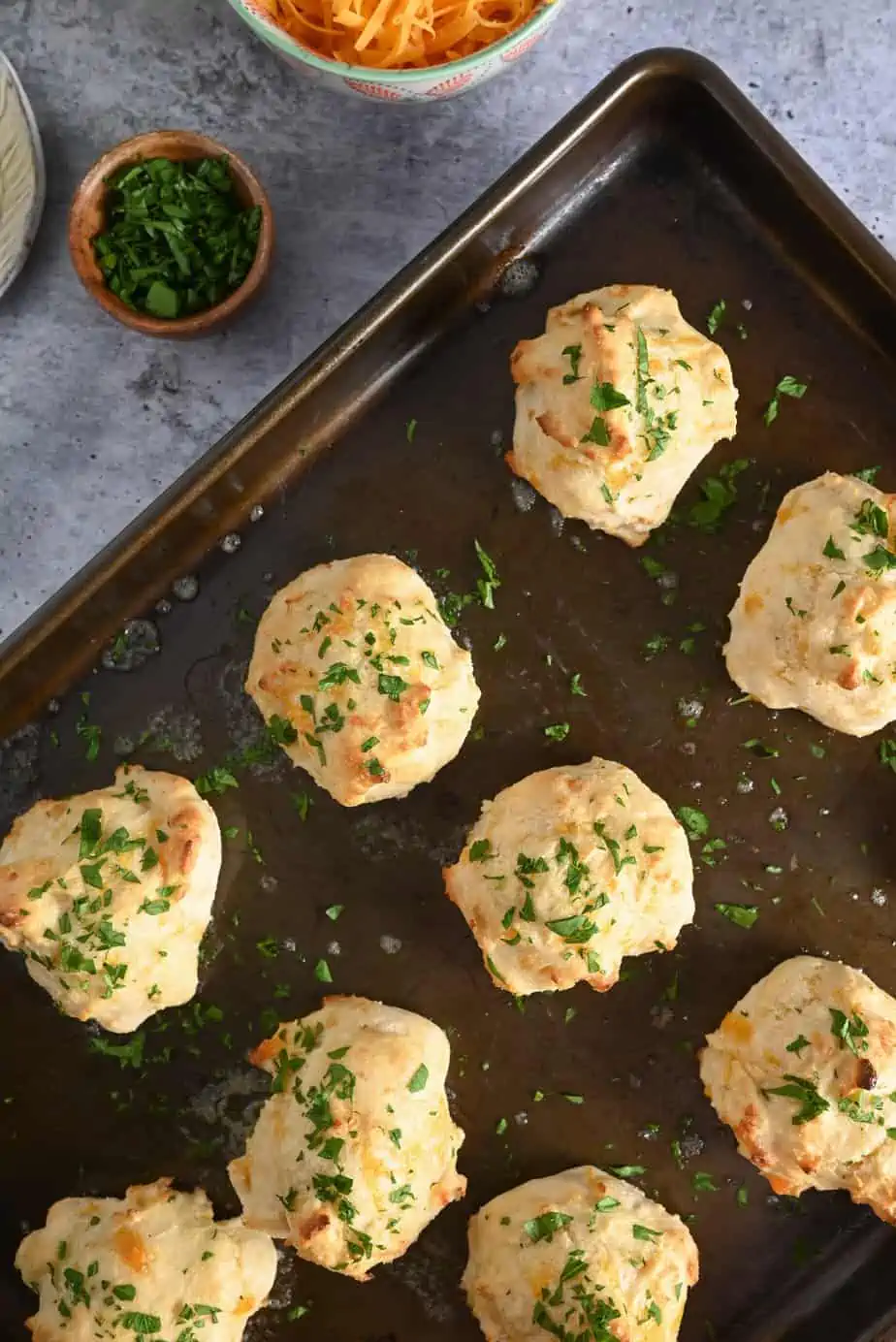 Overhead view of baked red lobster biscuits, topped with minced parsley, on a baking sheet.