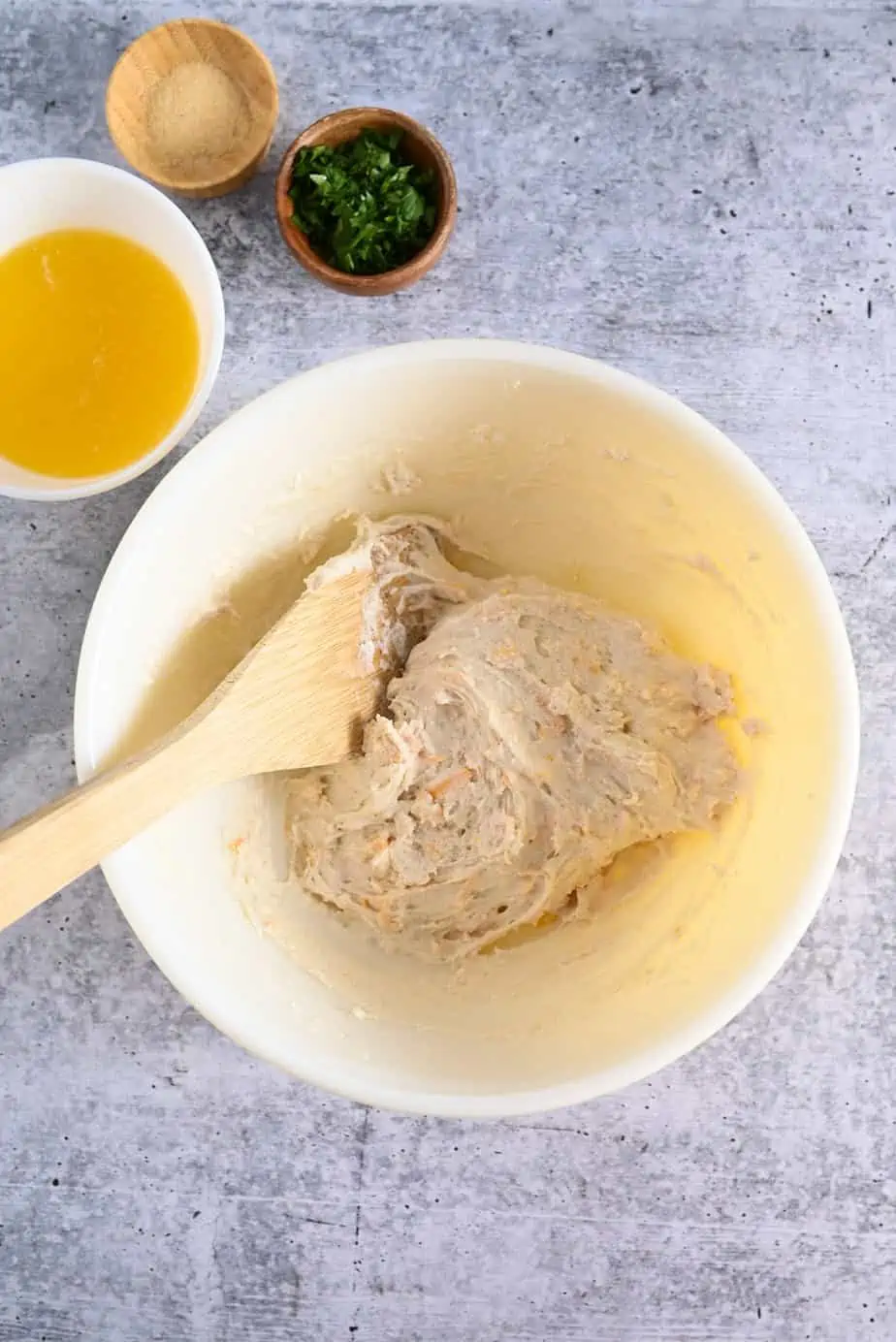 Red lobster biscuit dough being stirred with a wooden spoon in a white mixing bowl.