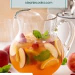 Side view of a glass pitcher filled with white peach sangria and garnished with sprigs of mint. Text overlay includes recipe name.