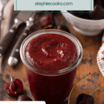 Glass jar filled with cherry barbecue sauce with a bowl of sweet cherries in the background. Text overlay includes recipe name.
