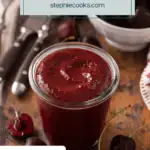 Glass jar filled with cherry barbecue sauce with a bowl of sweet cherries in the background. Text overlay includes recipe name.
