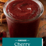 Close up of cherry barbecue sauce on a wooden board with pulled pork sandwiches in the background. Text overlay includes recipe name.
