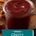 Close up of cherry barbecue sauce on a wooden board with pulled pork sandwiches in the background. Text overlay includes recipe name.