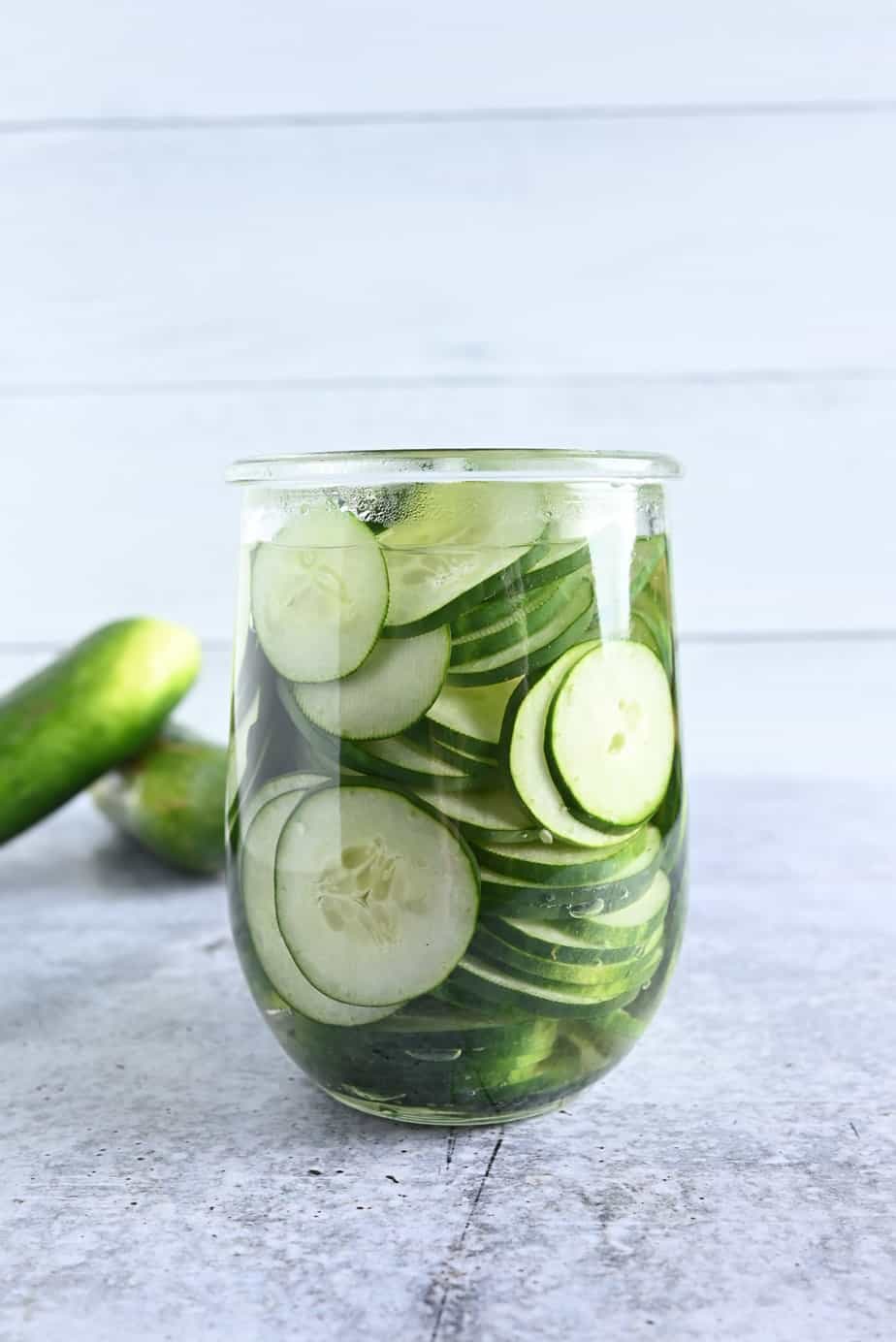 Sliced cucumbers covered with pickle brine in an open glass jar.