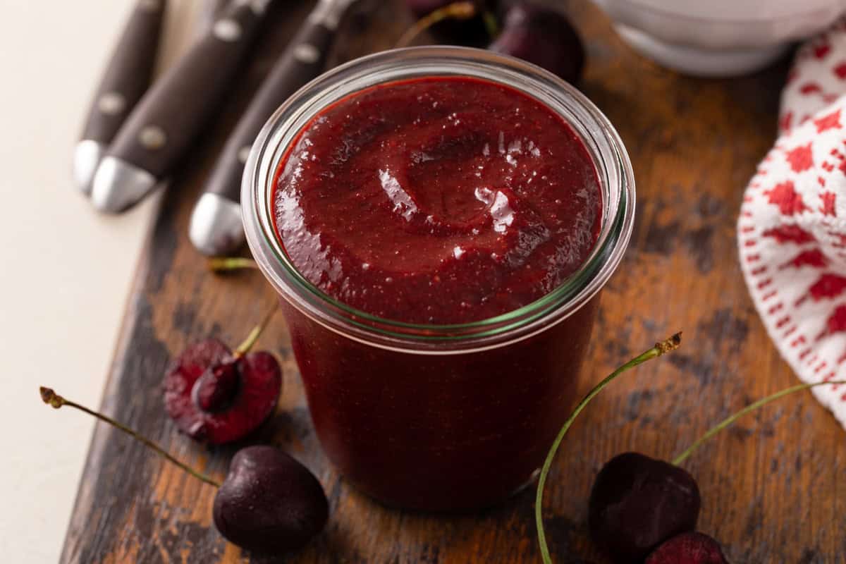 Jar of cherry barbecue sauce set on a wooden board.