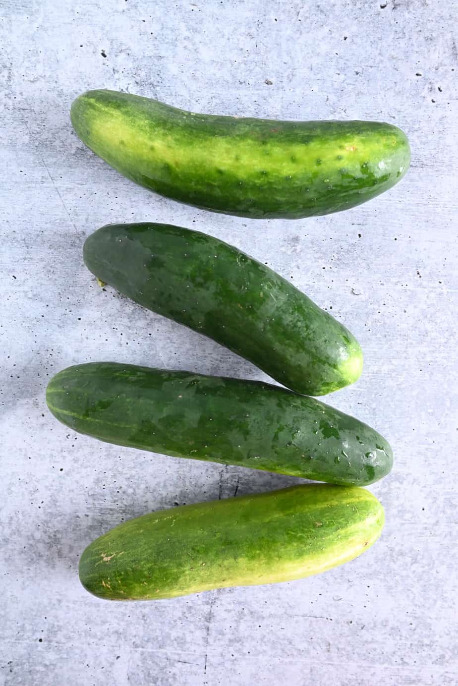 Four cucumbers arranged on a concrete countertop.