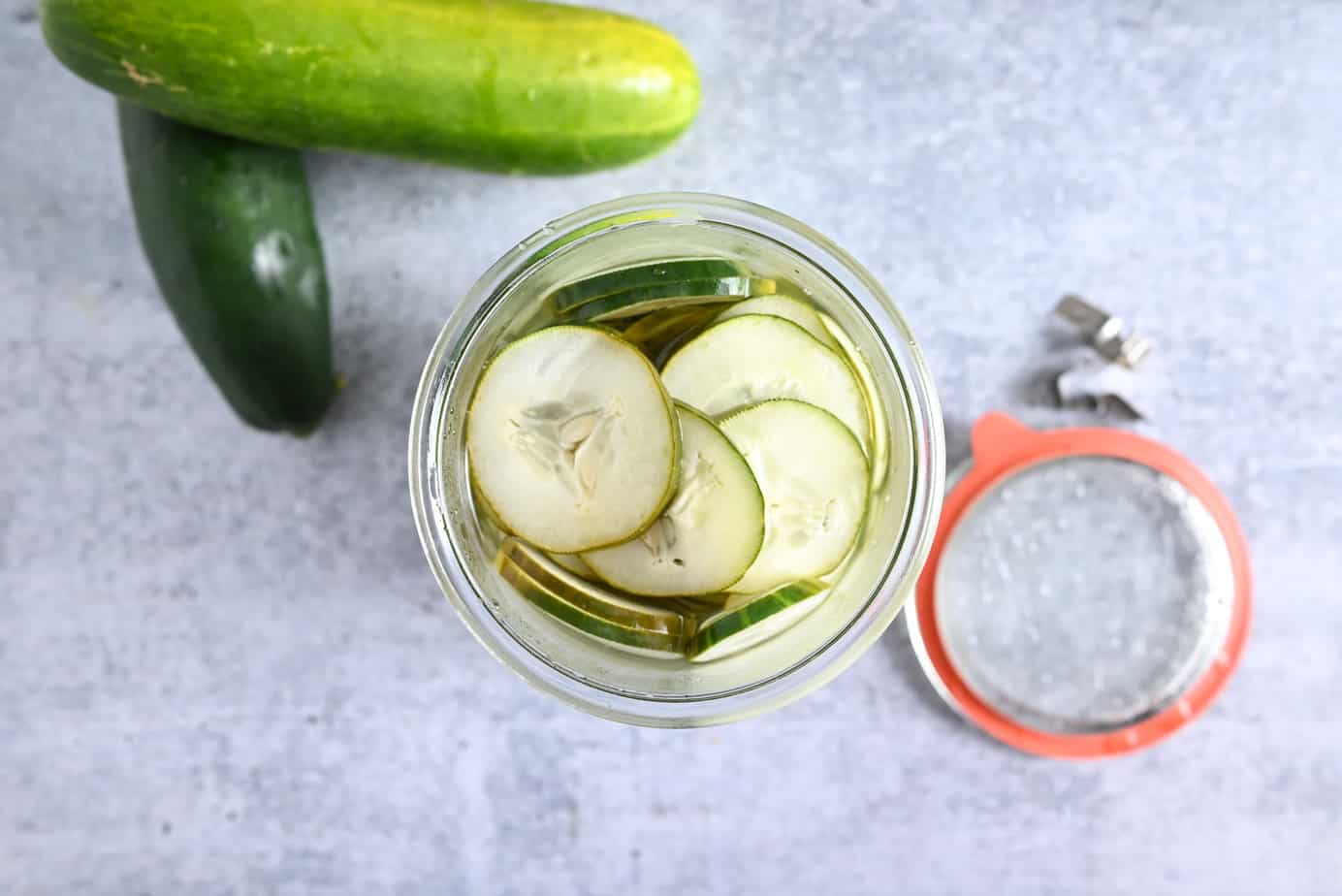 Overhead view of brined pickled cucumbers in a glass jar.