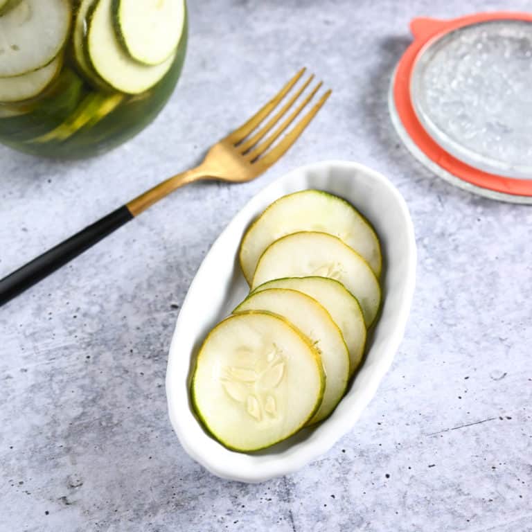 Close up of pickled cucumbers in a white dish on a concrete countertop.