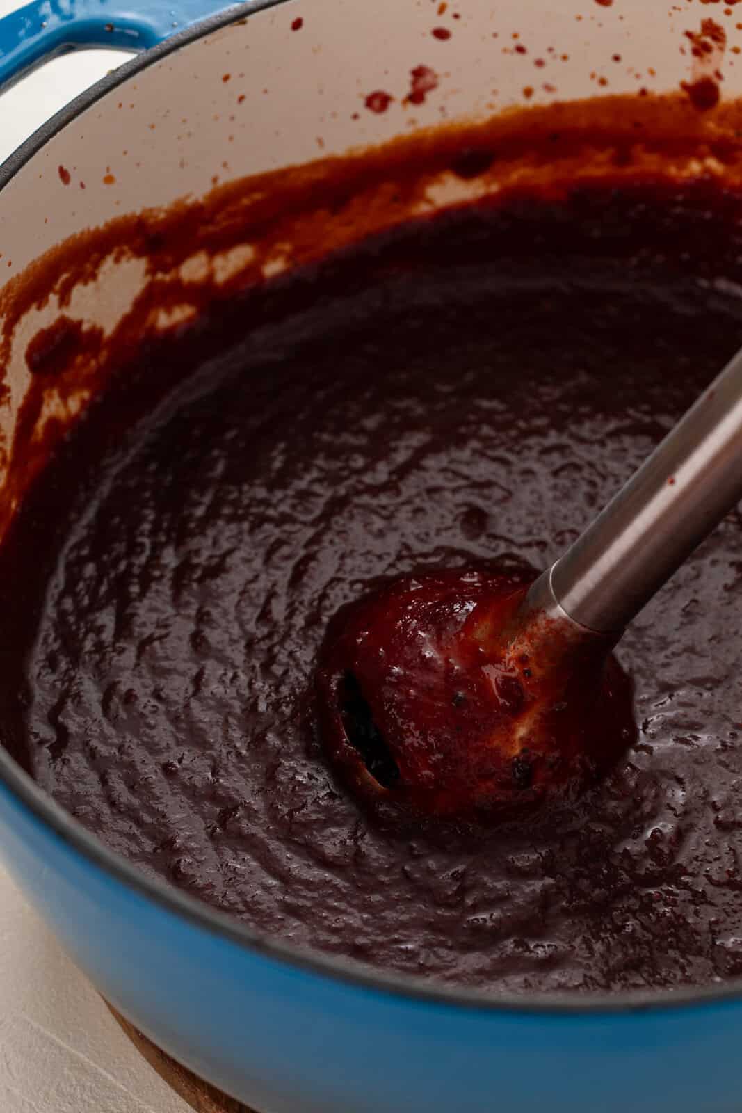 Cherry barbecue sauce being pureed with an immersion blender.