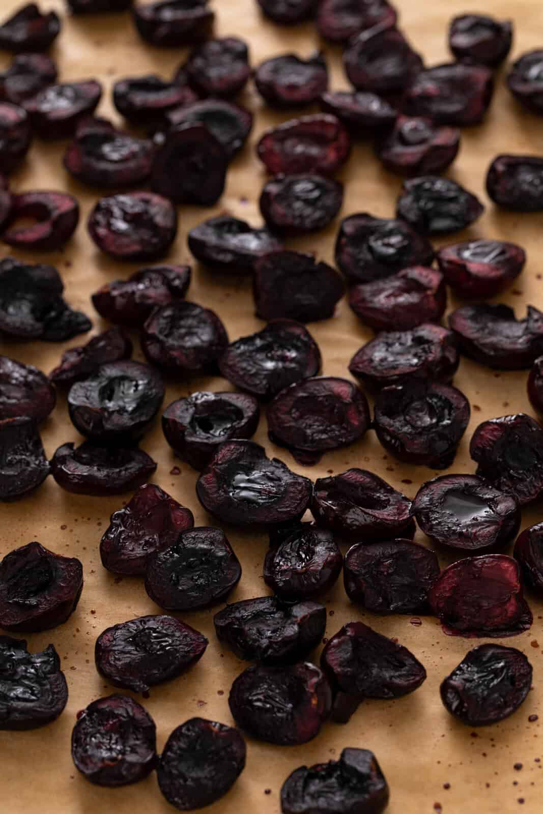 Close up of roasted sweet cherries on a parchment-lined pan.
