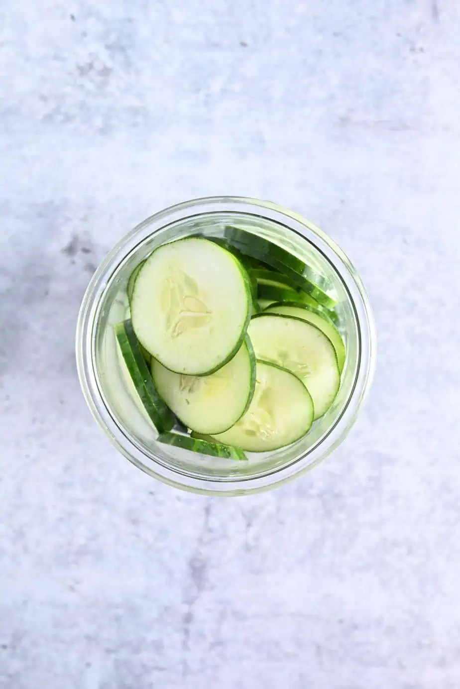 Overhead view of sliced cucumbers in a glass jar.