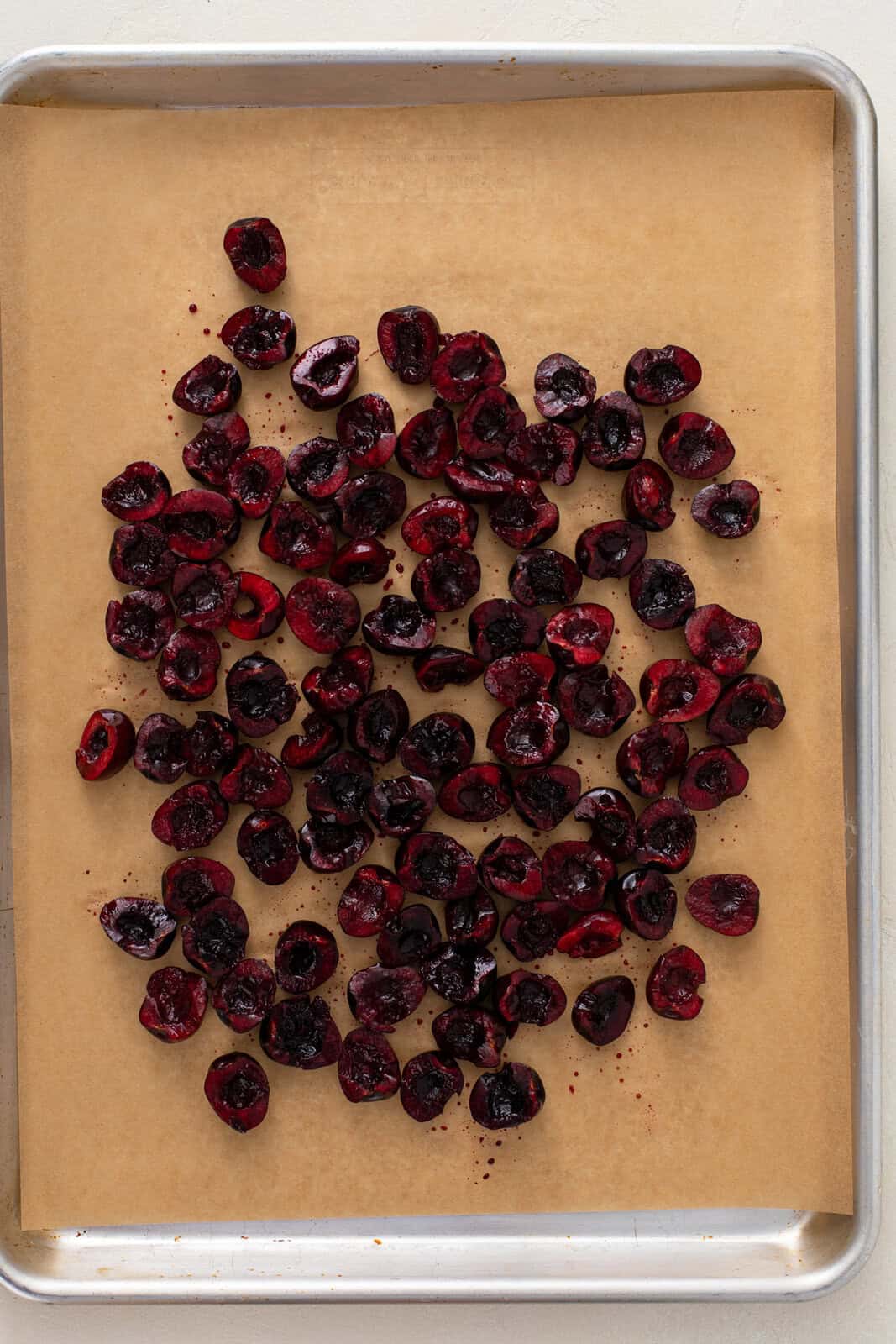 Pitted and halved sweet cherries on a parchment-lined sheet pan.
