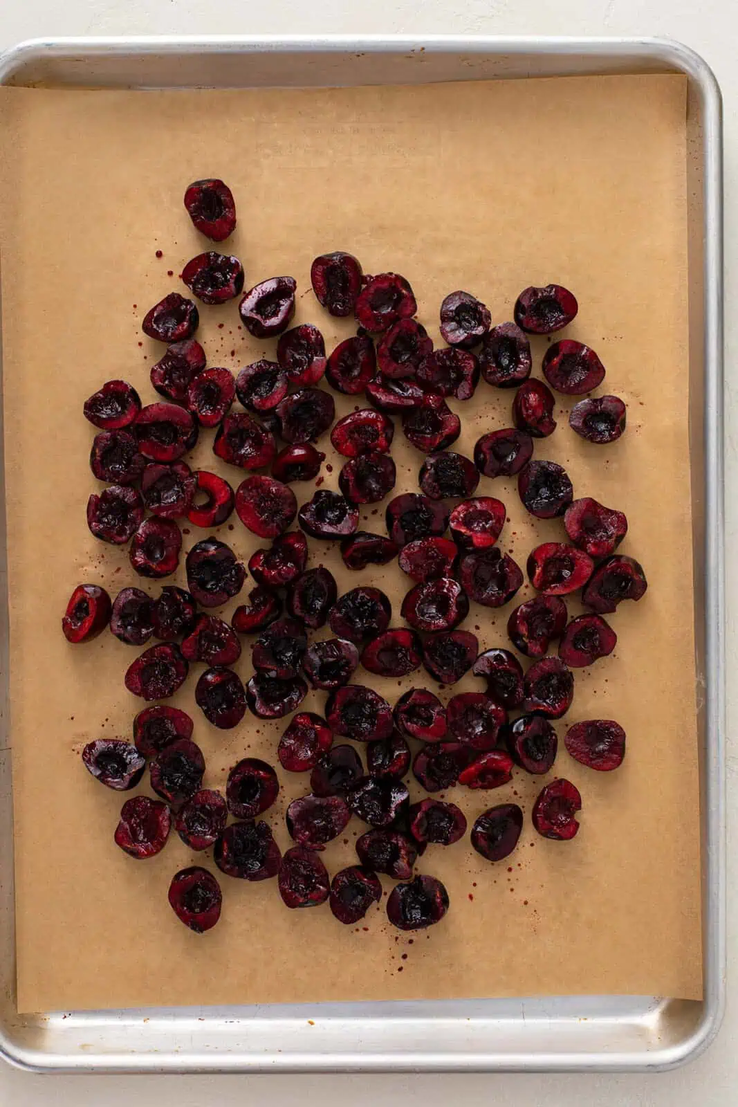Pitted and halved sweet cherries on a parchment-lined sheet pan.