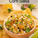 Hand squeezing fresh lime over a bowl of roasted corn salsa. Text overlay includes recipe name.