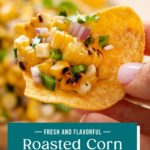 Hand holding up a tortilla chip topped with roasted corn salsa. Text overlay includes recipe name.