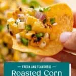 Hand holding up a tortilla chip topped with roasted corn salsa. Text overlay includes recipe name.