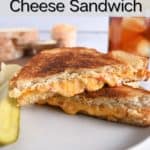 Side view of two halves of a grilled pimento cheese sandwich stacked on a white plate. A glass of iced tea is visible in the background. Text overlay includes recipe name.