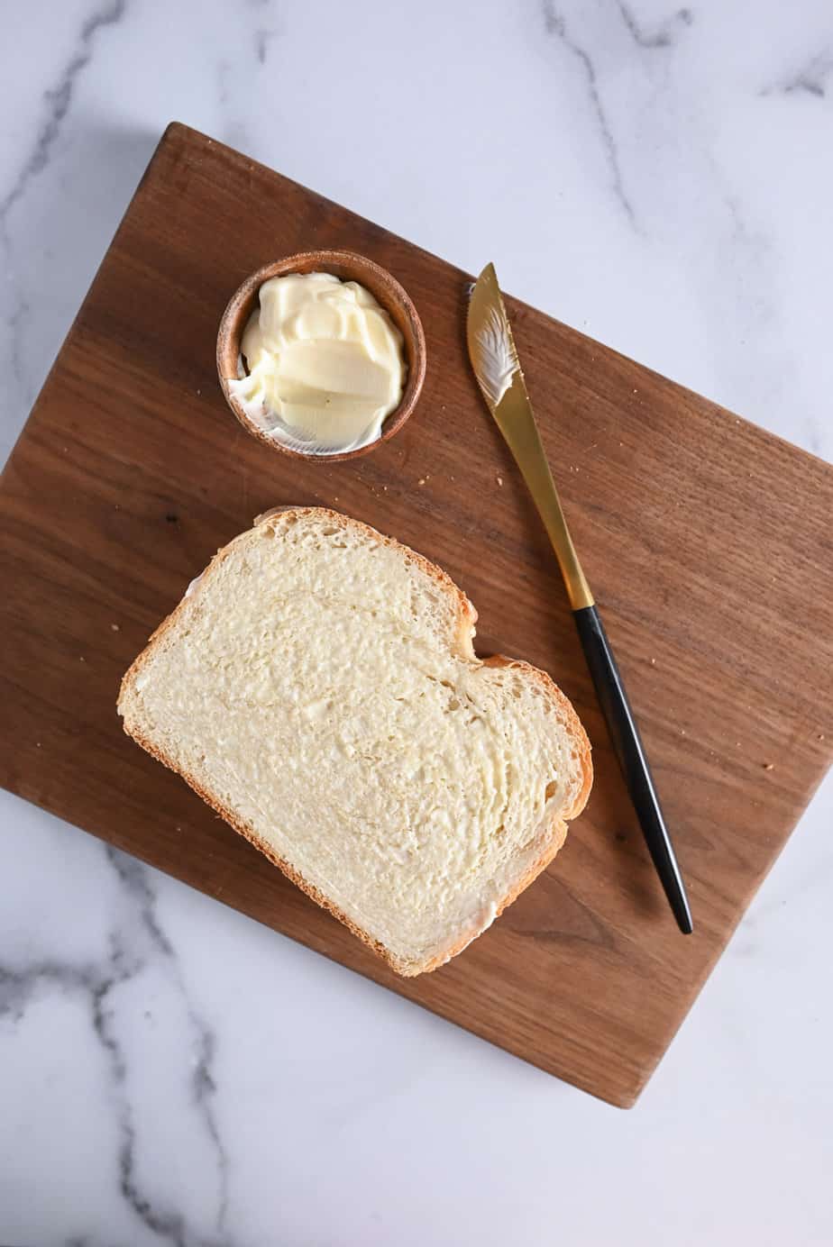 Assembled grilled pimento cheese sandwich on a wooden cutting board next to a butter knife and a small bowl of mayo.