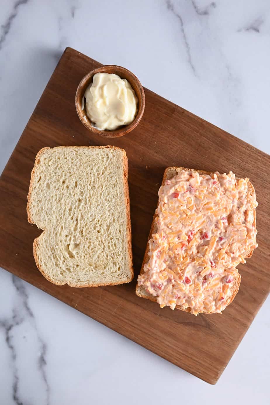 Pimento cheese spread onto a slice of sourdough bread on a wooden cutting board.