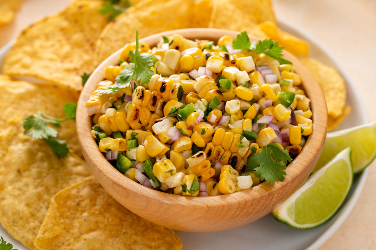 Close up image of a bowl of roasted corn salsa surrounded by tortilla chips.