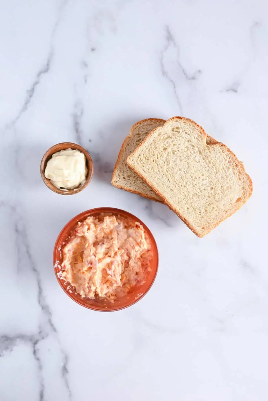 Ingredients for a grilled pimento cheese sandwich on a marble countertop.