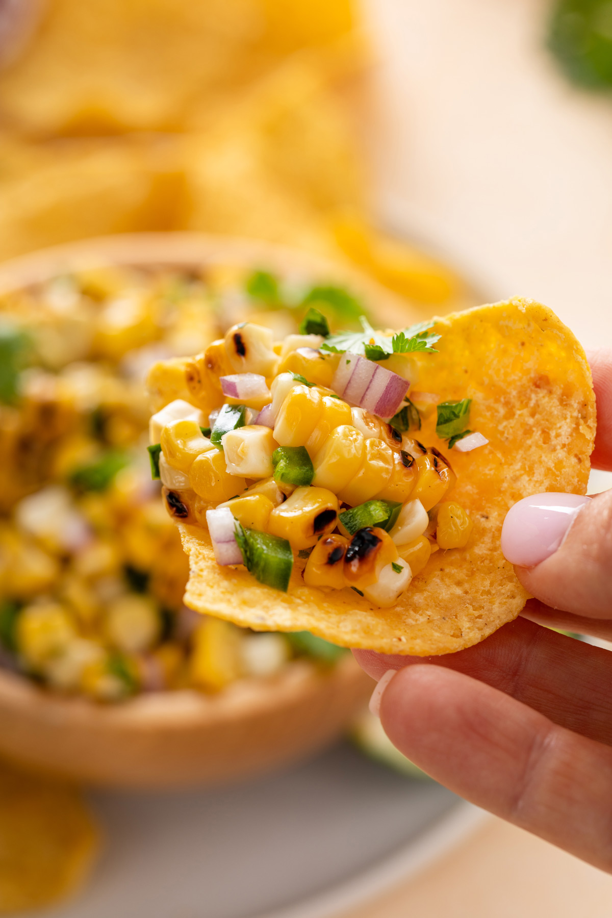 Hand holding up a tortilla chip topped with roasted corn salsa.