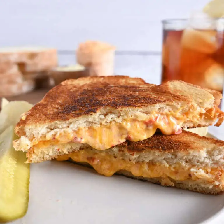 Grilled pimento cheese sandwich sliced in half on a white plate.