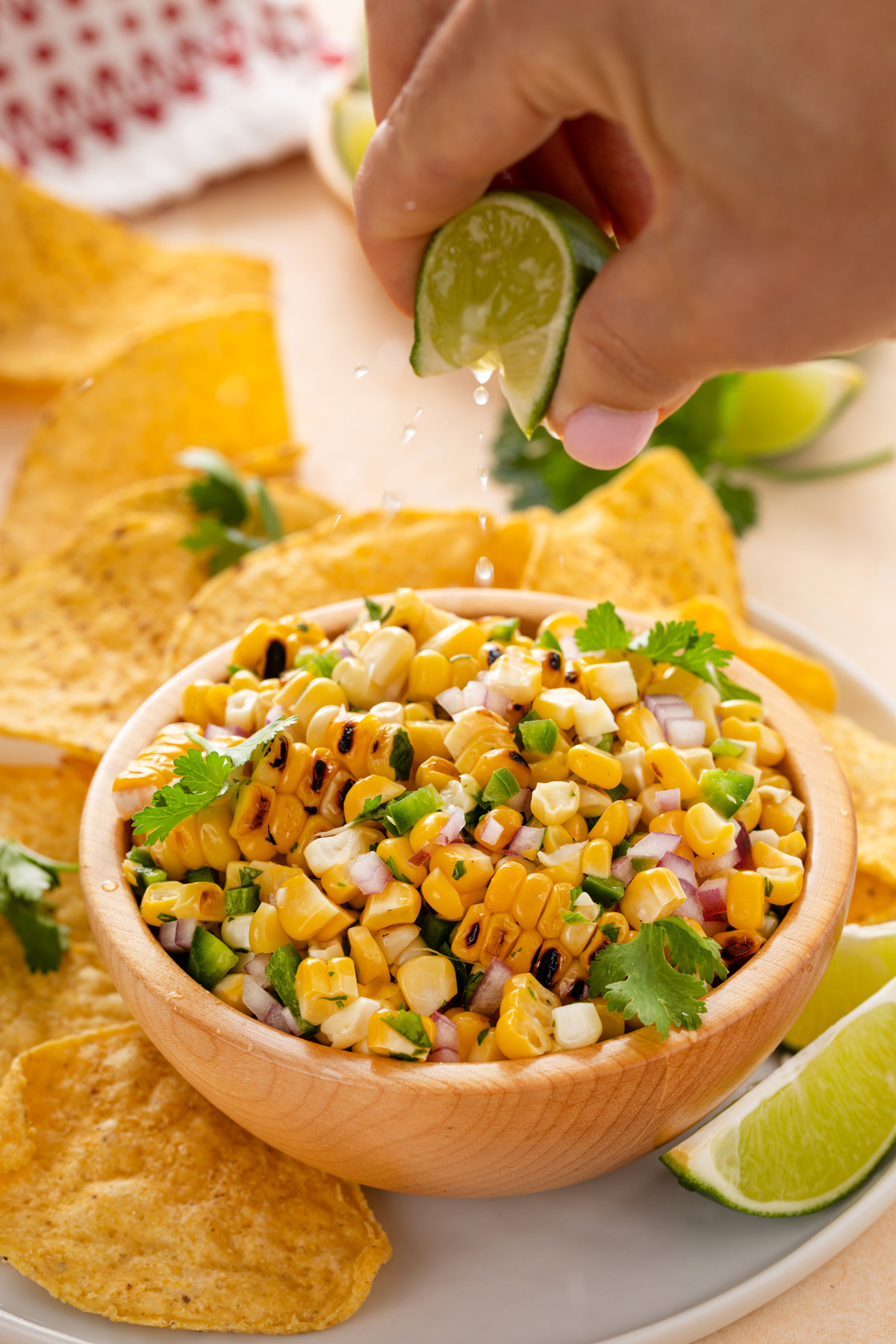 Hand squeezing fresh lime over a bowl of roasted corn salsa.
