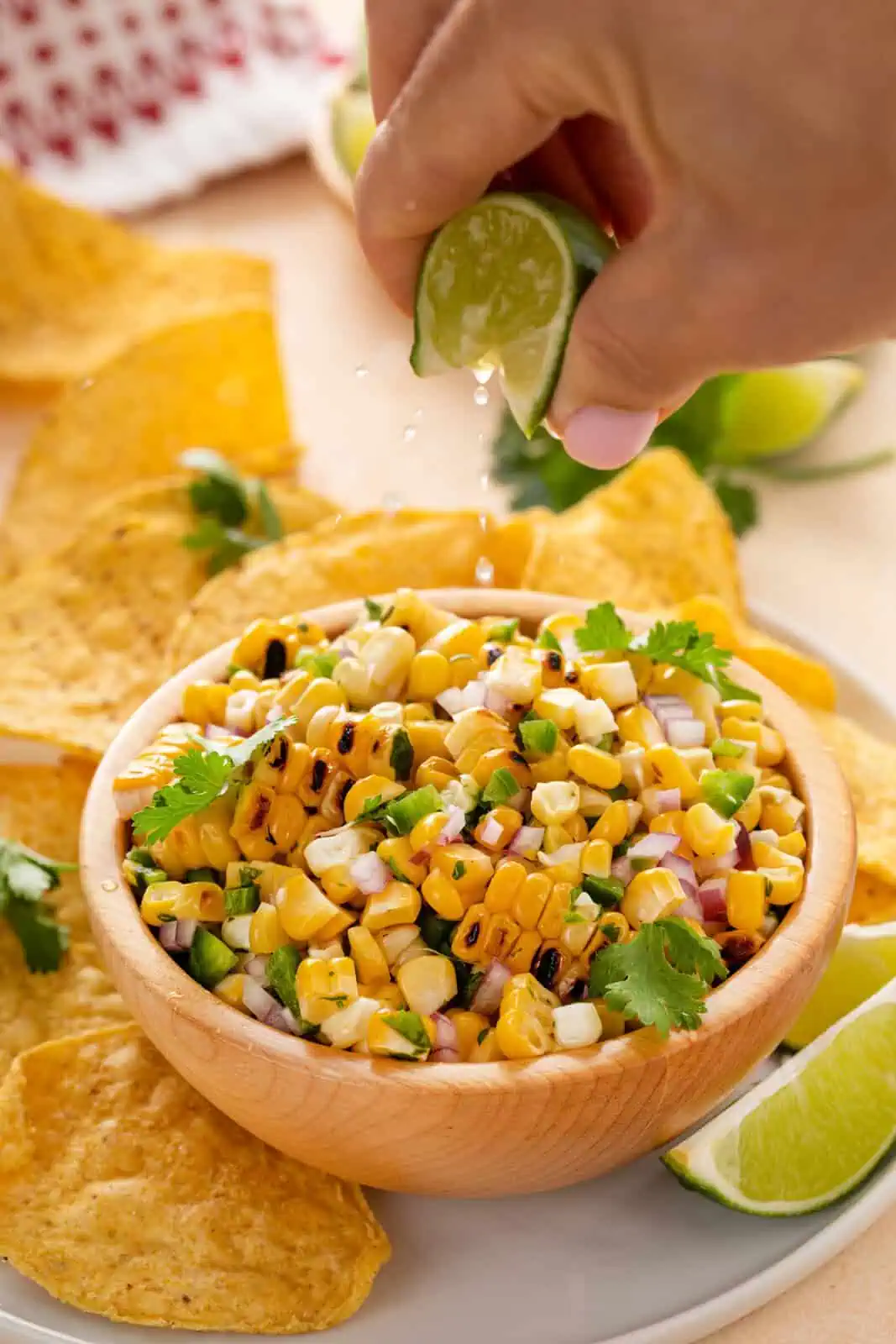 Hand squeezing fresh lime over a bowl of roasted corn salsa.