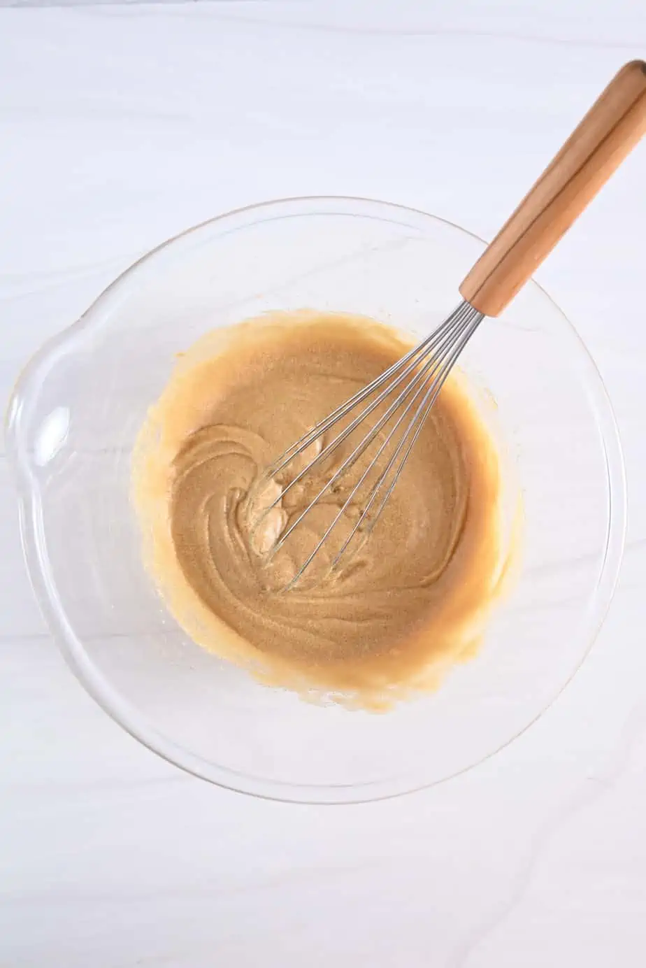 Wet ingredients for maple walnut blondies being whisked together in a glass mixing bowl.